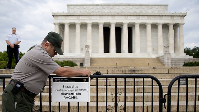 A US Park Police officer watches at left as a National Park Service employee posts a sign on a barricade closing access to the Lincoln Memorial in Washington.