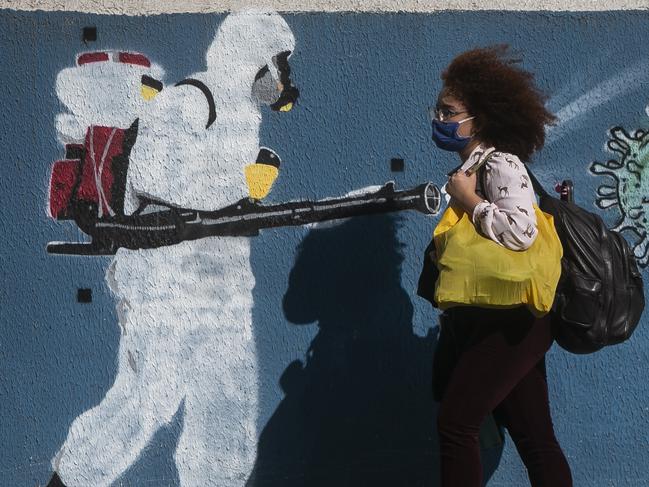 RIO DE JANEIRO, BRAZIL - JUNE 08: A woman wearing a mask walks past a wall with a graffiti depicting a cleaner in protective gear spraying viruses with the face of President Jair Bolsonaro in Estacio neighborhood amidst the coronavirus (COVID-19) pandemic on June 8, 2020 in Rio de Janeiro, Brazil. (Photo by Bruna Prado/Getty Images)