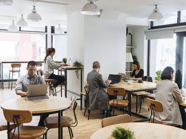 Coworkers sitting at tables independently and using laptops, digital nomad, hot desking, freelancing