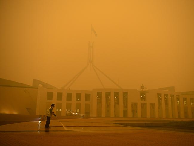 A man cleans the forecourt of Parliament House surrounded by smoke haze early morning in Canberra, Sunday, January 5, 2020. (AAP Image/Lukas Coch) NO ARCHIVING