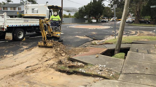 A Sydney Water emergency repair crew cleans up the soil and rubble left after a water main burst smashed through the footpath at the corner of Parr and Waratah parades at Narraweena. Picture: Jim O'Rourke