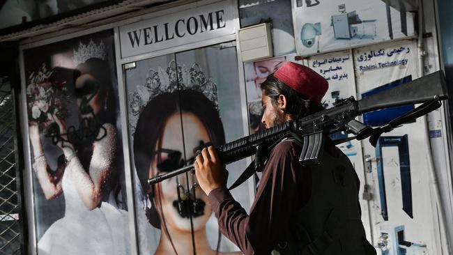 A Taliban fighter walks past a beauty salon with images of women defaced using a spray paint in Kabul. Picture: Wakil Kohsar/AFP