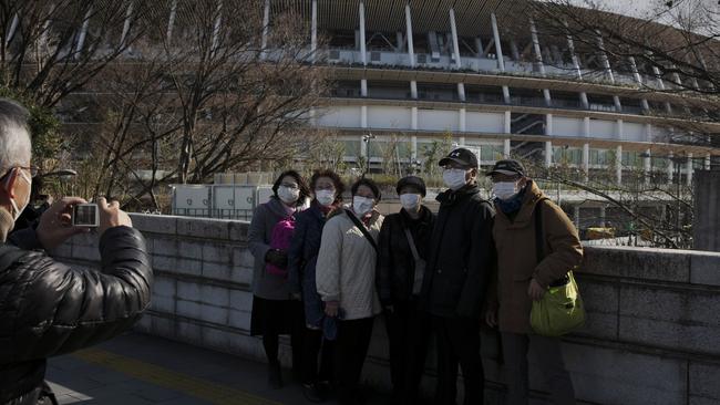 Tourists wear masks as they pause for photos with the New National Stadium, a venue for the opening and closing ceremonies at the Tokyo 2020 Olympics. Picture: Jae C Hong/AP