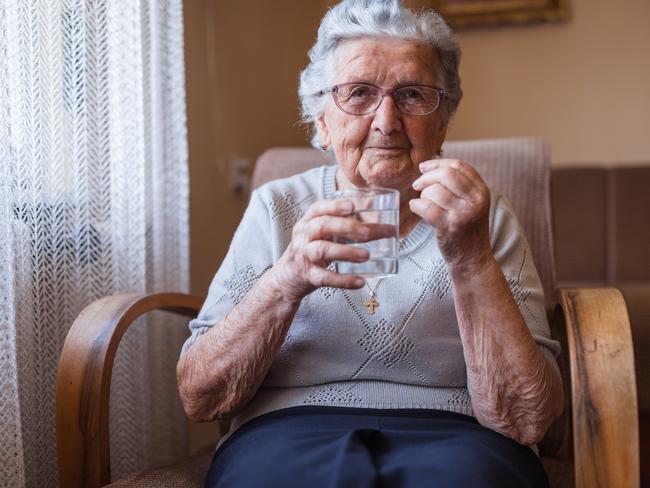 Happy old lady holding glass of water when resting at home