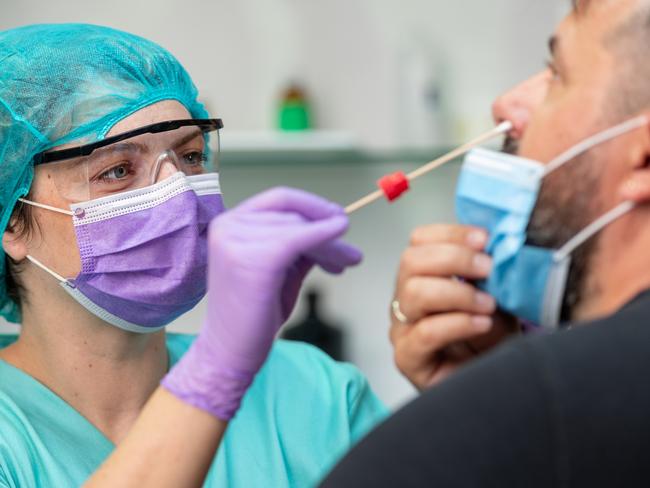 Female doctor in protective workwear taking nose swab test from middle aged man wearing protective face mask, Covid-19 pandemic outbreak