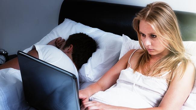 A handsome young couple lie in bed; she's intent on her laptop, either keeping up with social media, working late, or battling insomnia; he's fast asleep next to her. Istock