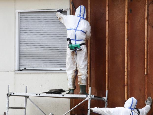 Professionals in protective suits remove asbestos on a wall