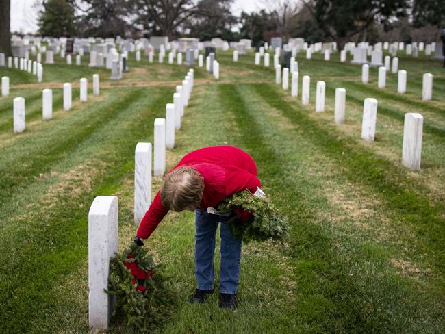 ARLINGTON, VA - DECEMBER 18: A woman places a wreath on a tombstone at Arlington National Cemetery, on December 18, 2021 in Arlington, Virginia. The 30th annual Wreaths Across America project places wreaths on the more than 250,000 tombstones of military servicemen and women at Arlington National Cemetery.   Al Drago/Getty Images/AFP == FOR NEWSPAPERS, INTERNET, TELCOS & TELEVISION USE ONLY ==