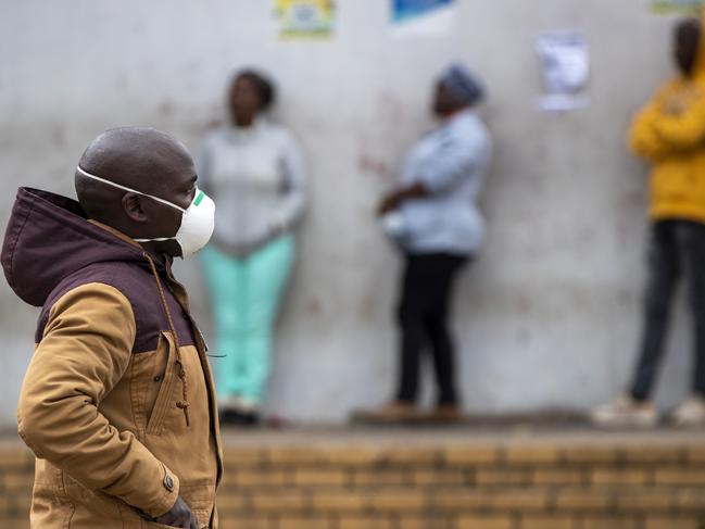 A man wearing a face mask walks past people queuing for shopping in Duduza, east of Johannesburg, South Africa. Picture: AP