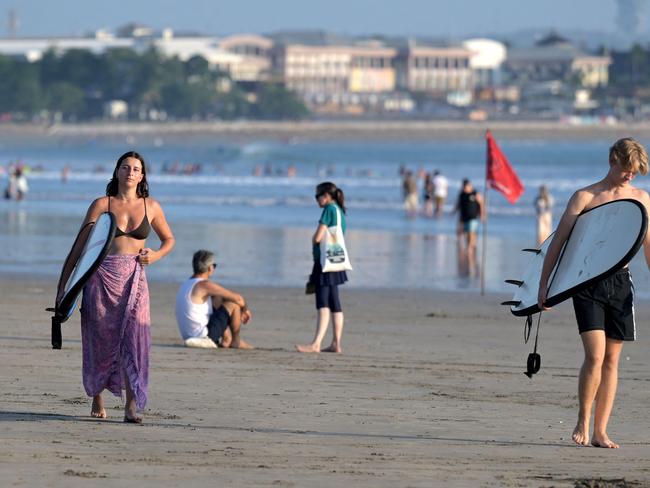 Foreign tourists carry their surfboard as they walk along Kuta beach near Denpasar, on Indonesia's Bali island on August 3, 2024. (Photo by SONNY TUMBELAKA / AFP)