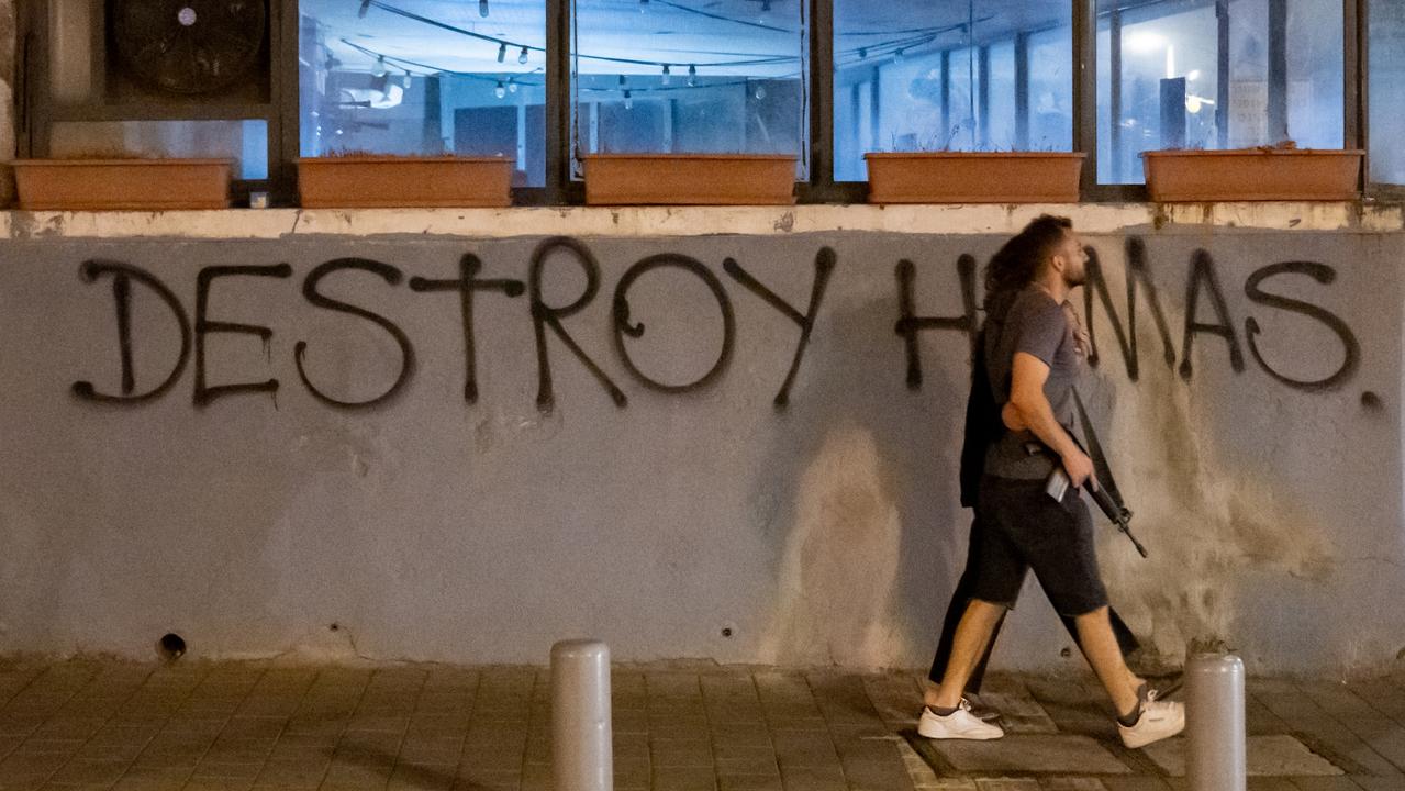 A person carrying a gun, with his arm around a woman walks past a spray painted sign that reads "Destroy Hamas" in Tel Aviv. Picture: Getty