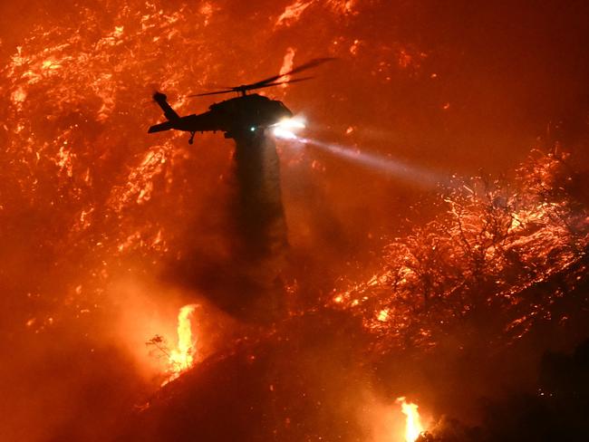 A fire fighting helicopter drops water as the Palisades fire grows near the Mandeville Canyon neighborhood and Encino, California, on January 11, 2025. The Palisades Fire, the largest of the Los Angeles fires, spread toward previously untouched neighborhoods January 11, forcing new evacuations and dimming hopes that the disaster was coming under control. Across the city, at least 11 people have died as multiple fires have ripped through residential areas since January 7, razing thousands of homes in destruction that US President Joe Biden likened to a "war scene." (Photo by Patrick T. Fallon / AFP)