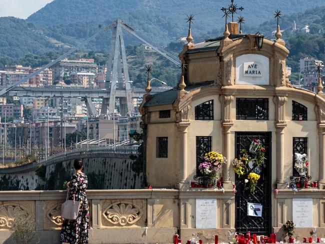 A stretch of the Morandi Bridge stands as a woman pauses beside tributes left for the victims of those killed when a section of the bridge collapsed. Picture: Getty Images