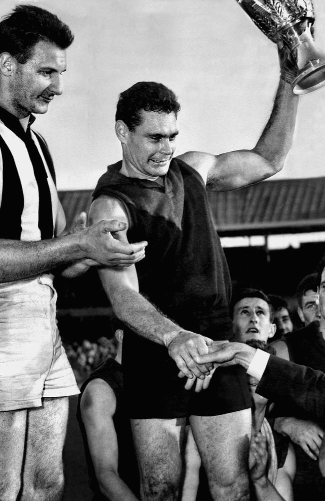 Ron Barassi holds up the 1964 premiership cup alongside Ray Gabelich.