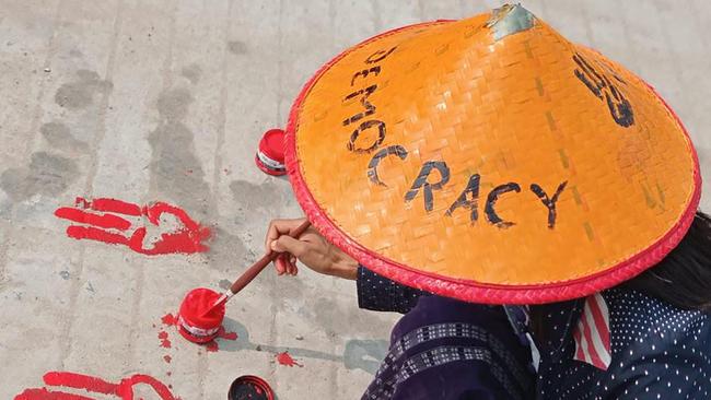 A protester painting the symbols of the three finger salutes on the ground with red paint as part of a "bleeding strike" demonstration against the military coup in Shwebo in Myanmar's Sagaing region. Picture: AFP