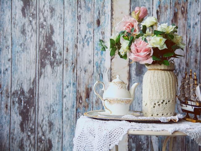 Porcelain teapot and cup on a table with a vase with artificial flowers on a background of the old wooden walls. Small boat on the table