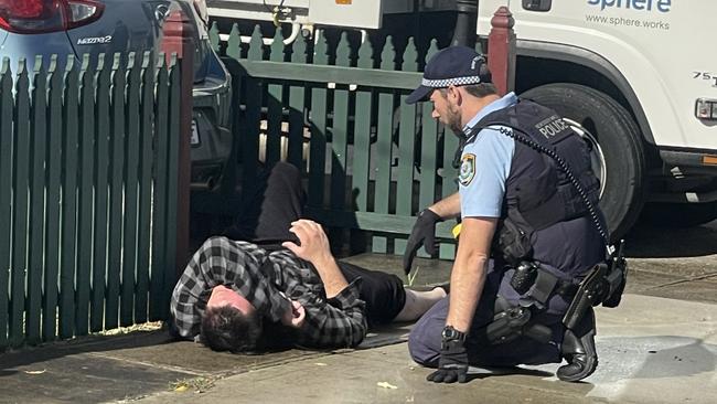 At one point the upset man lay on the footpath, as he was spoken to by a police officer. Picture: The Daily Telegraph