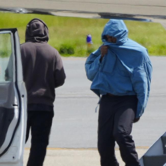 Kanye West tries to hide his face as he exits the aircraft. Picture: The Image Direct