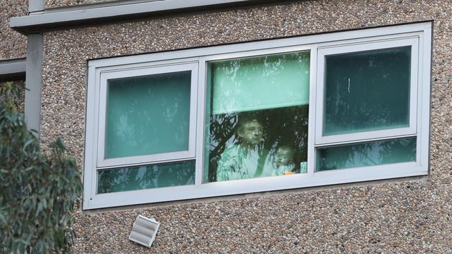 Residents peer out the windows at the public housing towers on Racecourse Rd in Flemington which have been locked down by the Victorian Government. Picture: David Crosling