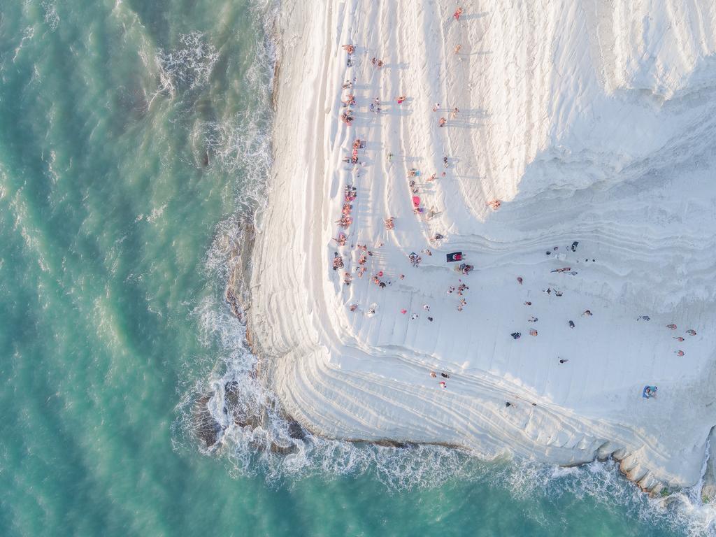 The Big Meringue ... Scala dei Turchi (The Turkish Steps) is a white cliff in Realmonte (Sicily), made of a soft limestone and a blinding white marl. Natural erosion has created steps on the cliff face, making it look soft and sinuous, like a big meringue covered with sprinkles (the people sitting and walking on it). Scala dei Turchi is a wonderful spot for viewing the sunset, as the bright white marl turns into a strong orange. Only after shooting this image, while watching it on a bigger screen, I noticed a newlywed couple in the frame kissing for their wedding photoshoot. Exactly at the edge of the cliff. Picture: Placido Faranda, Italy, Entry, Open, Landscape &amp; Nature (2018 Open competition), 2018 Sony World Photography Awards