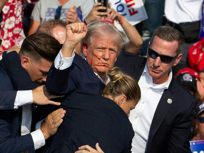 TOPSHOT - Republican candidate Donald Trump is seen with blood on his face surrounded by secret service agents as he is taken off the stage at a campaign event at Butler Farm Show Inc. in Butler, Pennsylvania, July 13, 2024. Donald Trump was hit in the ear in an apparent assassination attempt by a gunman at a campaign rally on Saturday, in a chaotic and shocking incident that will fuel fears of instability ahead of the 2024 US presidential election. The 78-year-old former president was rushed off stage with blood smeared across his face after the shooting in Butler, Pennsylvania, while the gunman and a bystander were killed and two spectators critically injured. (Photo by Rebecca DROKE / AFP)