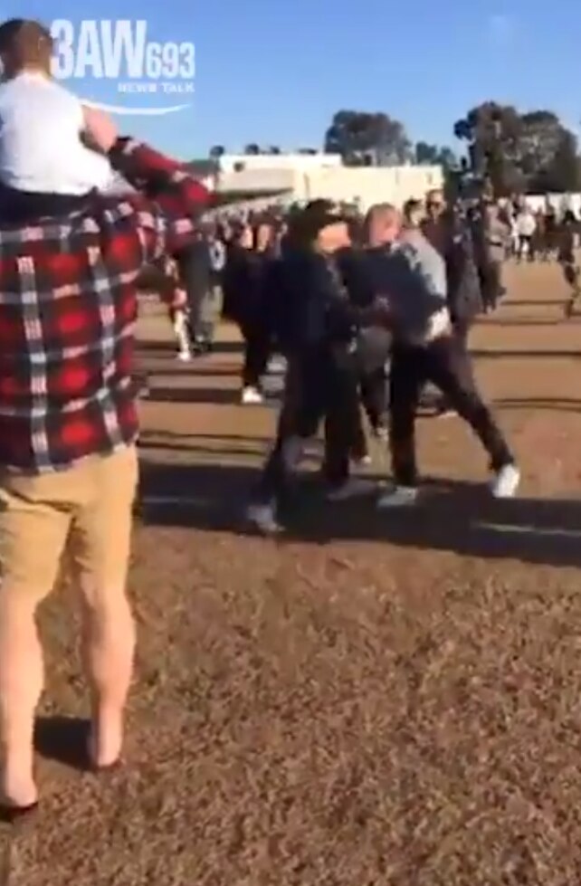 A man with a young child on his shoulders watches as two men confront each other. Courtesy: 3AW