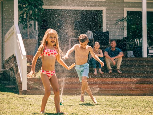 Family playing in the backyard, splashing in the sprinklers. Picture: iStock