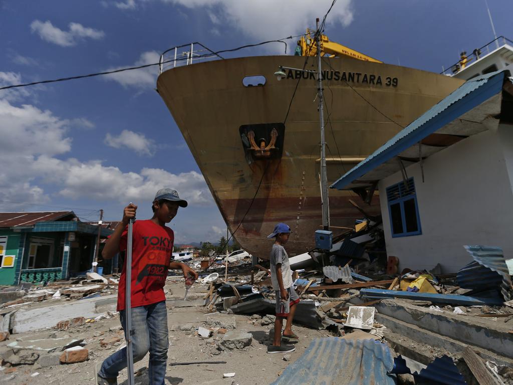 Indonesian youths walk past a ship that was swept ashore by the tsunami on the outskirts of Palu, Central Sulawesi, Indonesia. Picture: AP Photo/Dita Alangkara