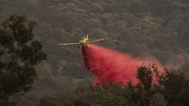 A small aircraft dumps fire retardant behind houses at the foot of Mount Tennant as the fire front of the Orroral Valley fire creeps through the Namadgi National Park. Picture: Getty