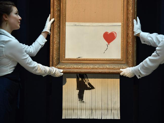 BEST NEWS PICTURES OF 2018 - -- AFP PICTURES OF THE YEAR 2018 -- Sotheby's employees pose with the newly completed work by artist Banksy entitled "Love is in the Bin", a work that was created when the painting "Girl with Balloon" was passed through a shredder in a surprise intervention by the artist, at Sotheby's auction house in London on October 12, 2018, following the work's sale. - The buyer of a work by street artist Banksy that was partially destroyed moments after it sold has gone through with the purchase, Sotheby's auction house said on October 11, 2018. The painting "Girl with Balloon" was passed through a shredder hidden in the frame just after it went under the hammer last week for £1,042,000 ($1.4 million, 1.2 million euros). The modified version has now been certified by Banksy's authentication body Pest Control as a new piece of work in its own right, entitled "Love is in the Bin". (Photo by Ben STANSALL / AFP) / RESTRICTED TO EDITORIAL USE - MANDATORY MENTION OF THE ARTIST UPON PUBLICATION - TO ILLUSTRATE THE EVENT AS SPECIFIED IN THE CAPTION