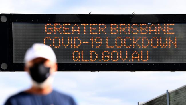 An electronic sign with a Covid message is seen as a man wears a face mask in Brisbane. Picture: NCA NewsWire / Dan Peled