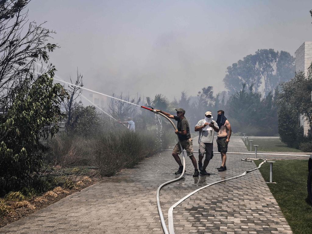 Residents use a hose to attempt to stop a fire from approaching houses. Picture: AFP