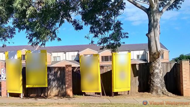 A photo of four real estate signs set up outside a property. Note: photo blurred.