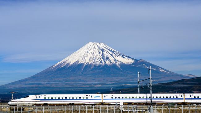 Fuji, Japan. A Shinkansen bullet train passes below Mt. Fuji through farmland. Doc Holiday Photo – iStock