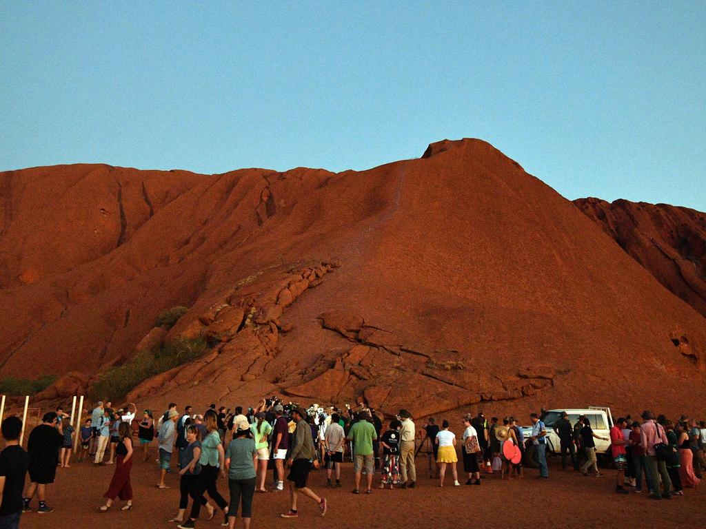 Tourists and residents are seen near Uluru, also known as Ayers Rock, following the day's close marking the start of a permanent ban on climbing the monolith, at Uluru-Kata Tjuta National Park in Australia's Northern Territory on October 25, 2019. - Australia's Uluru was permanently closed to climbers October 25 evening to meet the wishes of Aboriginal people who hold the red monolith sacred, but hundreds of tourists scaled it in the final hours before the ban. (Photo by Saeed KHAN / AFP)