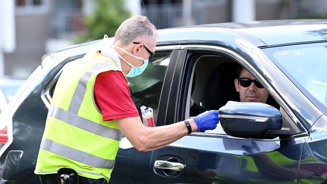 A health care worker is seen collecting information from people waiting in line to be COVID tested in Brisbane. Picture: Bradley Kanaris