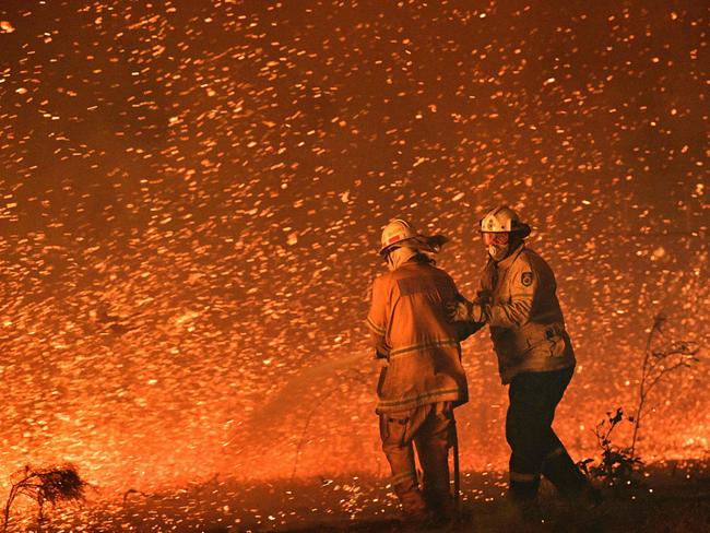 (FILES) This file picture taken on December 31, 2019 shows firefighters struggling against strong winds in an effort to secure nearby houses from bushfires near the town of Nowra in the Australian state of New South Wales. - Australia's unique wildlife is in retreat as it reels from bushfires, drought, human activity and global warming, according to a "shocking" government report on July 19, 2022 that prompted calls for dramatic change. (Photo by Saeed KHAN / AFP) / XGTY