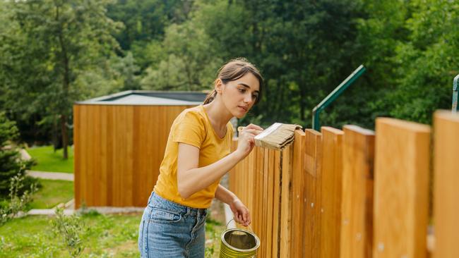 CAREERS: One side hustle is no longer enough to make ends meet, with a growing number of Australians requiring several income streams to pay their mortgage and put food on the table.  Photo of a young woman painting a garden fence. Picture: iStock