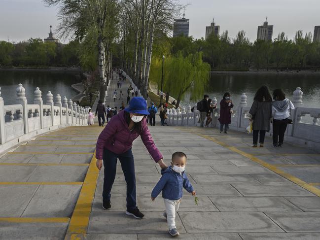 A woman and child wear protective masks as they cross a footbridge while enjoying the spring weather at a park in Beijing.