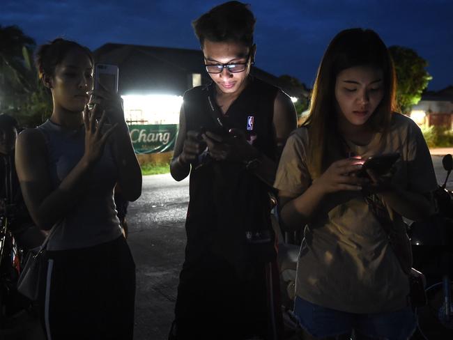 People anxiously check their mobile phones for updates while waiting at a military air base during the emergency helicopter evacuation to a hospital in Chiang rai. Picture: AFP Photo / Lillian Suwanrumpha