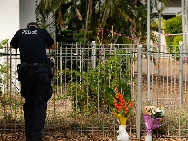 A weary NT police officer stands next to floral tributes at Gardens Hill Crescent where Nigel Hellings was killed. Picture: Glenn Campbell