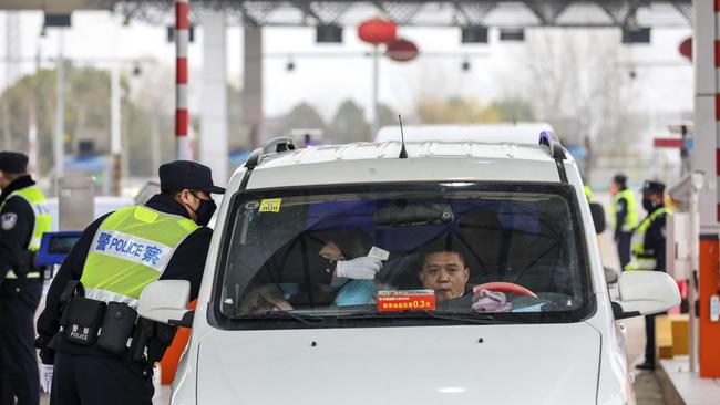 A policeman uses a digital thermometer to take a driver's temperature at a checkpoint at a highway toll gate in Wuhan in central China's Hubei Province, Chinatopix via AP