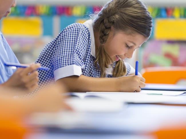 Students working at their desk. In focus is an Australian Aboriginal student very focussed on their books. Other children can also be seen in the classroom. Picture: Istock