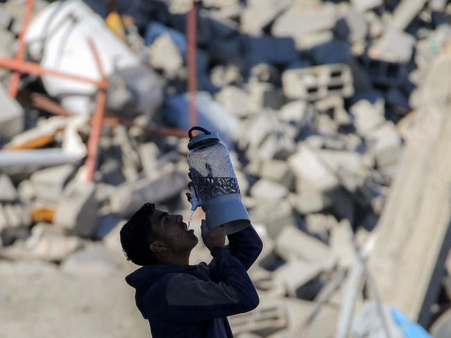 TOPSHOT - A boy drinks water from the tap of a dispenser in his hand by the rubble of a collapsed building in Rafah in the southern Gaza Strip on January 21, 2025, as residents return following a ceasefire deal in the war between Israel and Hamas in the Palestinian territory. (Photo by Eyad BABA / AFP)