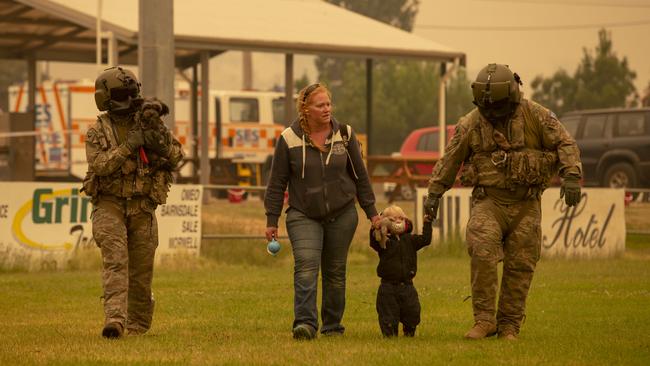 Two Australian Army Soldiers help people evacuate onto an Australian Army CH-47F Chinook helicopter at Omeo showgrounds, Victoria during support of Operation Bushfire Assist 19-20.