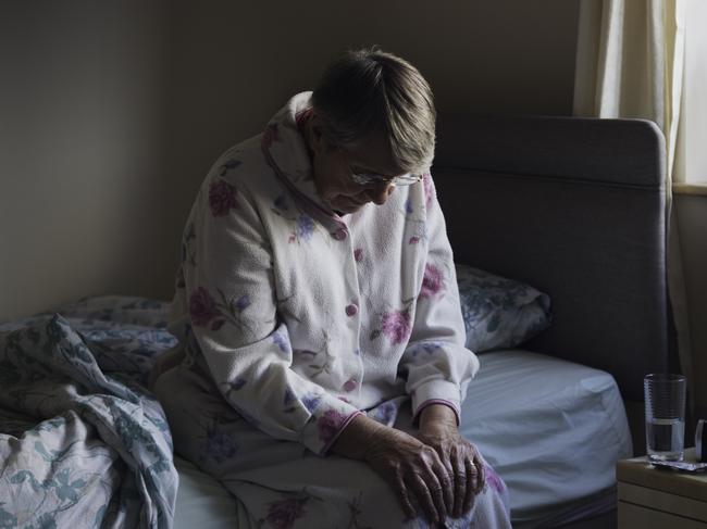 BAD AGED CARE:   A shot of a senior woman sitting on the side of her bed with her head down looking sad. She looks like she has just woken up as is dressed in nightwear.