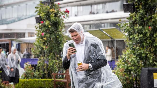 Many fashionistas were forced to cover their trackside outfits with raincoasts Picture: Jake Nowakowski