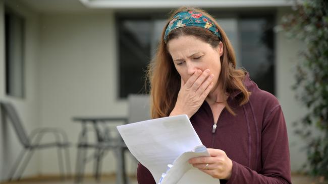 An upset adult woman (female age 25-35) reading a letter in home front yard.bill shock, woman shocked generic money