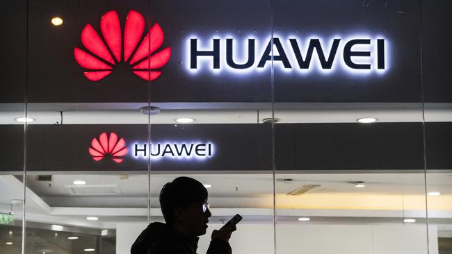 A pedestrian talks on the phone while walking past a Huawei store in Beijing. Picture: Getty Images