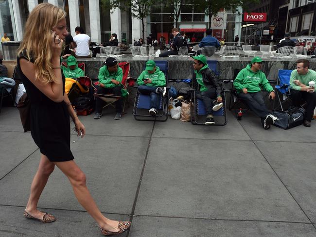 A woman on a cell phone walks by as people wait in line on chairs September 9, 2014 outside the Apple Store on 5th Avenue in New York. Tech trend-setter Apple charts its future course Tuesday amid expectations for new big-screen iPhones and possibly an 